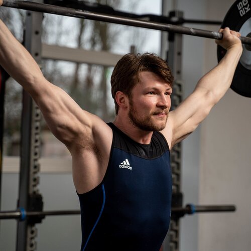 Alex Dear pressing a barbell overhead in a weightlifting singlet